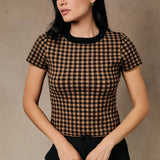 A woman wears a gingham sweater knit crew neck tee with a light brown and black plaid pattern.