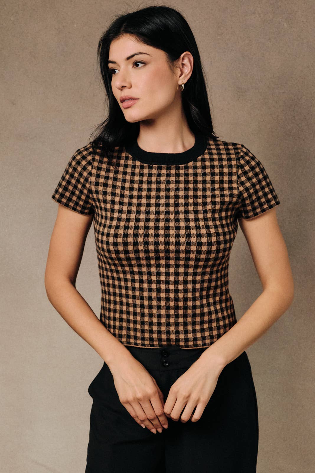 A woman wears a gingham sweater knit crew neck tee with a light brown and black plaid pattern.