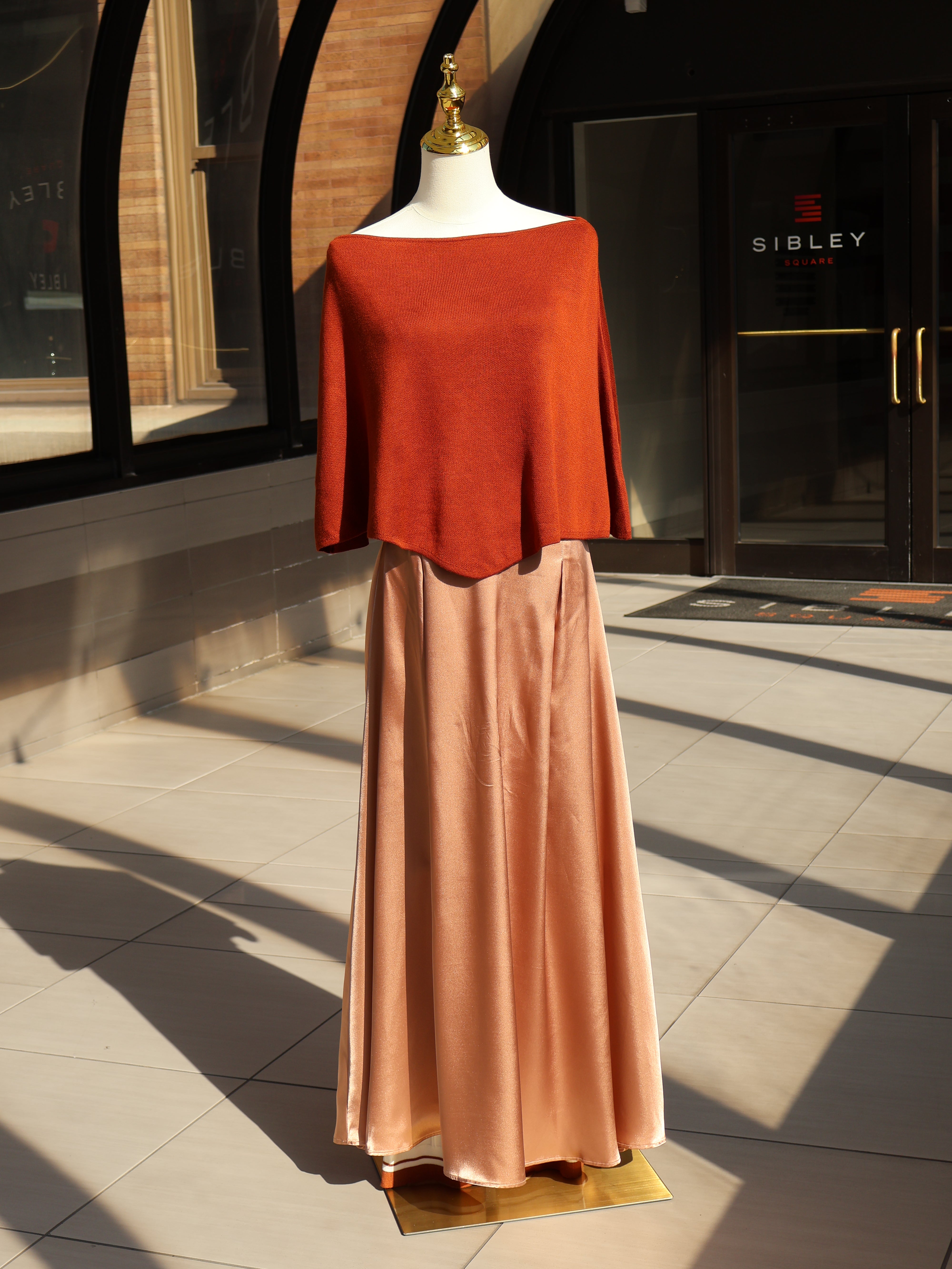Orange poncho knit top with a slouchy neckline displayed on a mannequin.