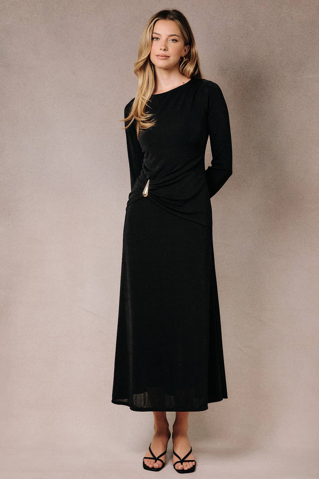 Black maxi dress with a boat neck, long sleeves, and a front ruched buckle detail worn by a model.