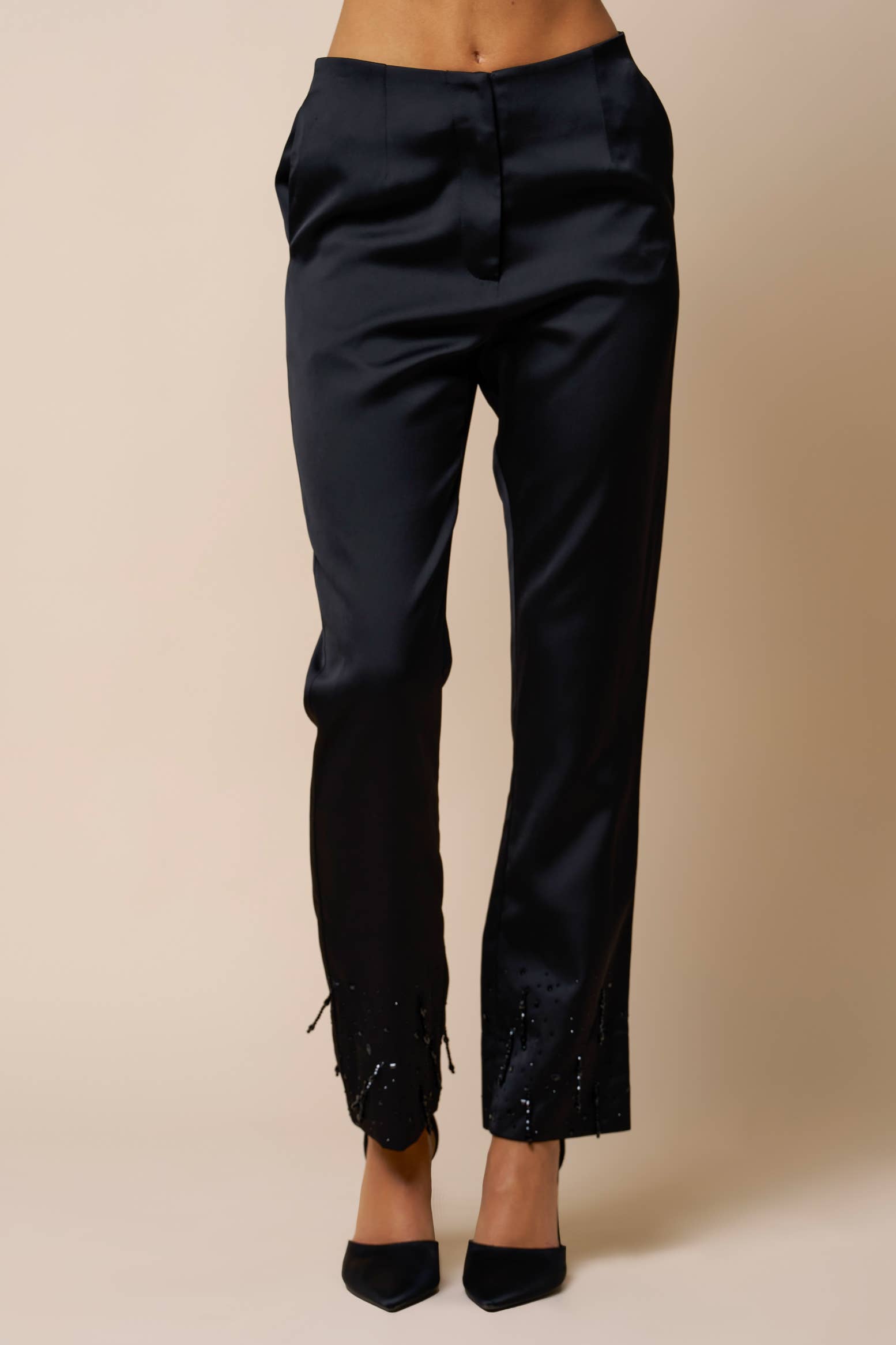 Black satin pants with beaded detailing at the ankles and functional side pockets.