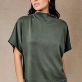 A woman wearing a rich olive green mock neck top with relaxed dolman sleeves.