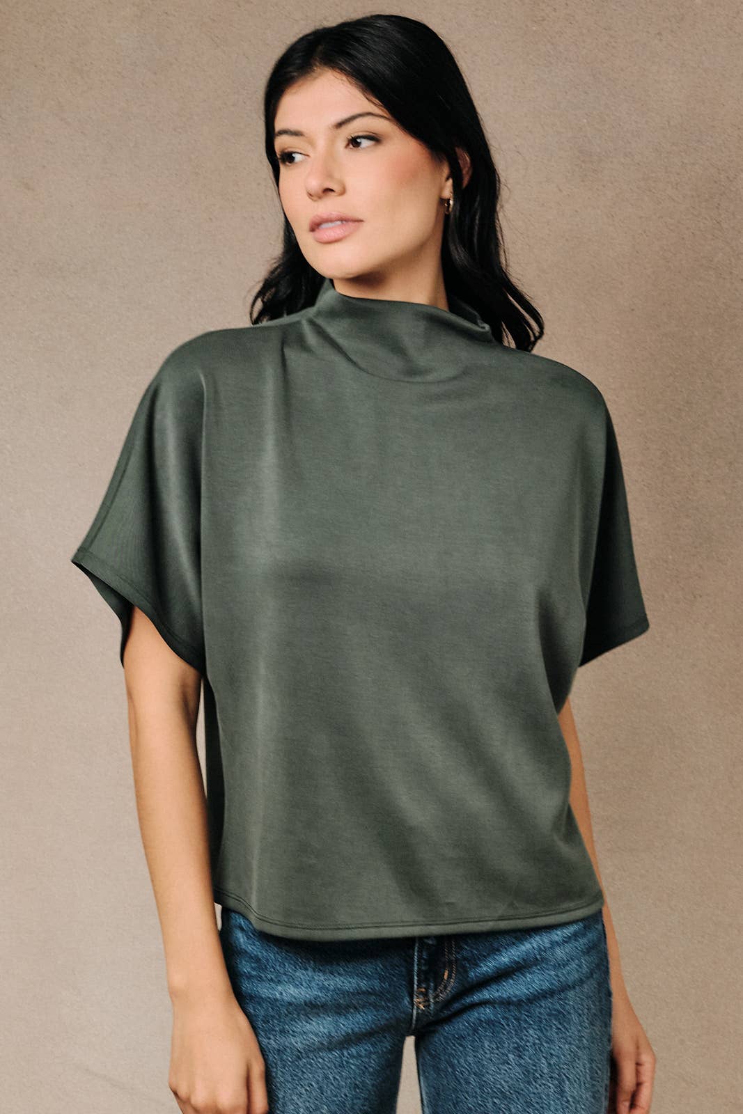 A woman wearing a rich olive green mock neck top with relaxed dolman sleeves.