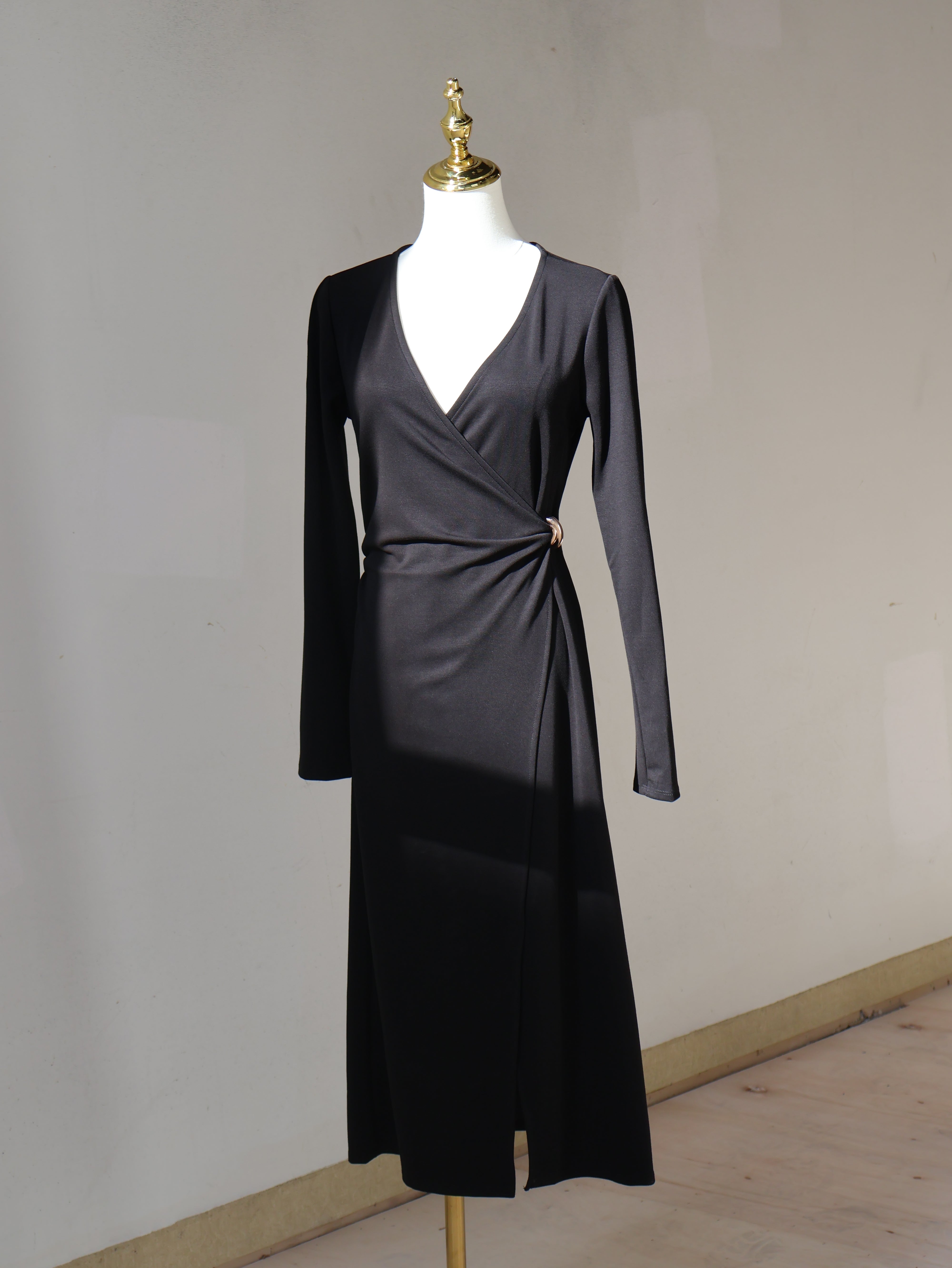 Black wrap midi dress with a V-neckline, long sleeves, and gold-tone waist accent displayed on a mannequin.