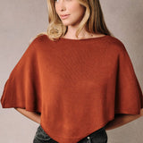 A woman wearing a rust-colored poncho knit top with a slouchy neckline.