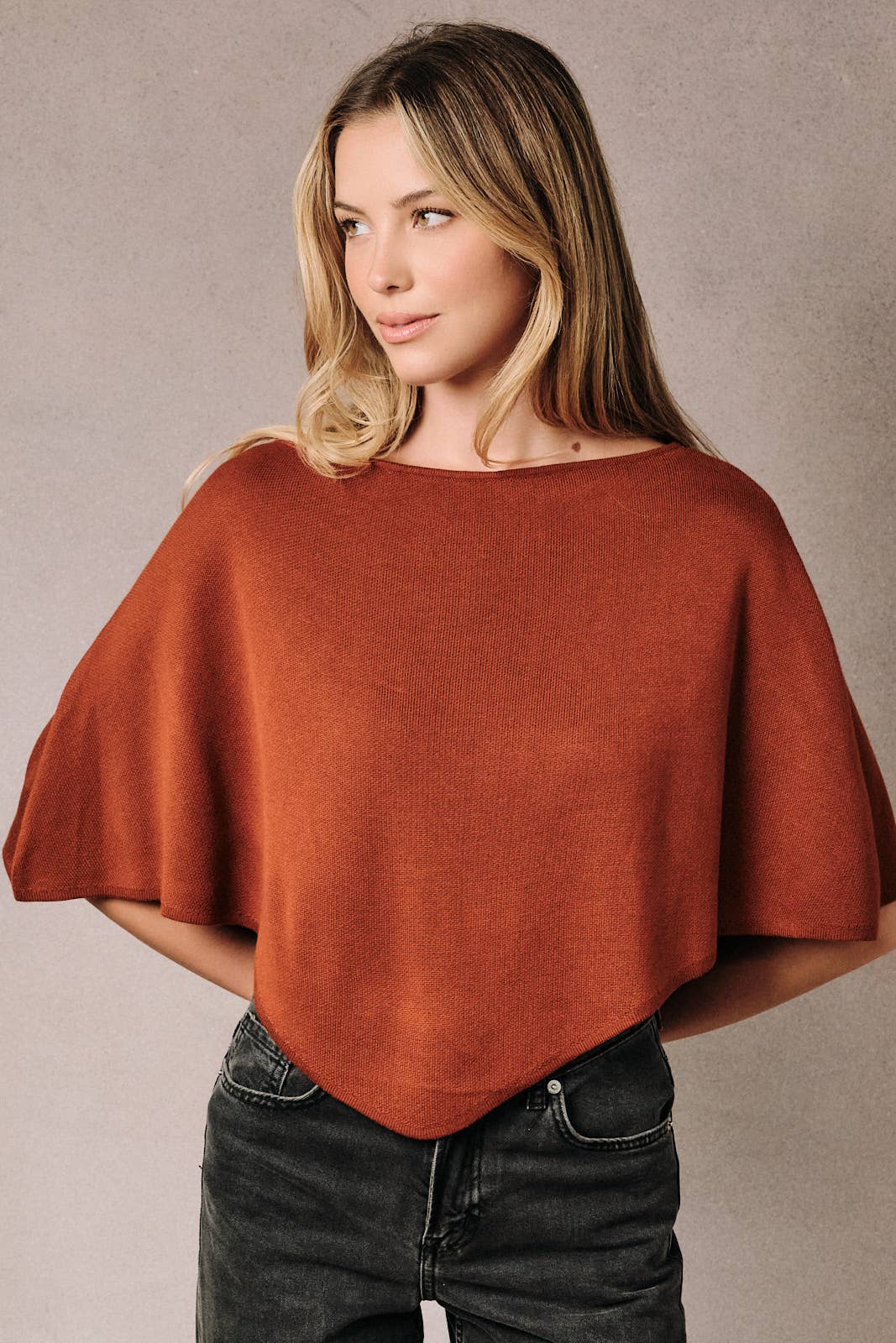 A woman wearing a rust-colored poncho knit top with a slouchy neckline.