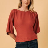 A rust-colored long sleeve top with a boat neck and back tie detail, worn by a model.