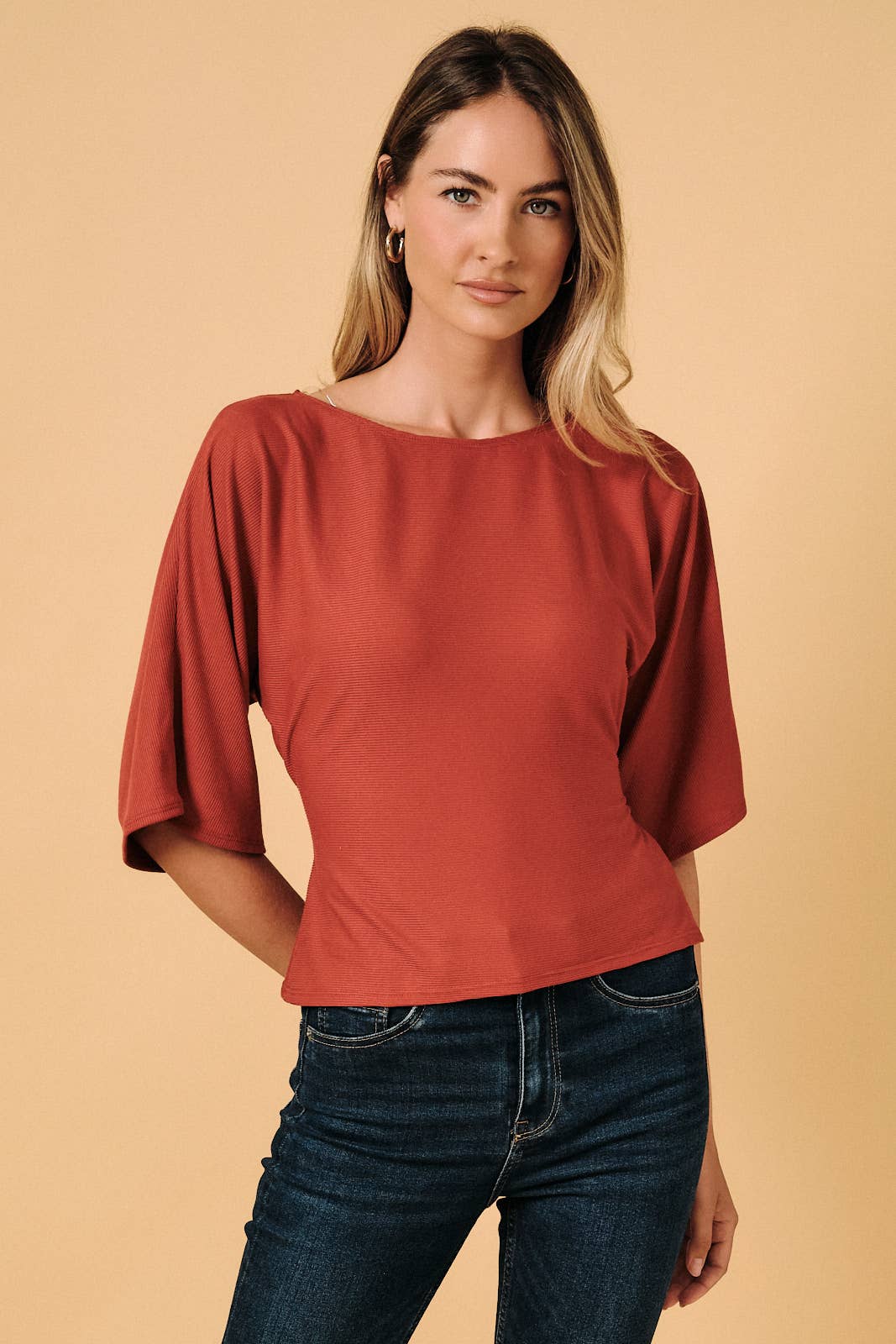 A rust-colored long sleeve top with a boat neck and back tie detail, worn by a model.
