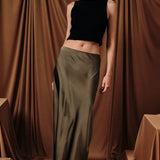 A bias-cut satin midi skirt in olive, worn by a model with a black top.