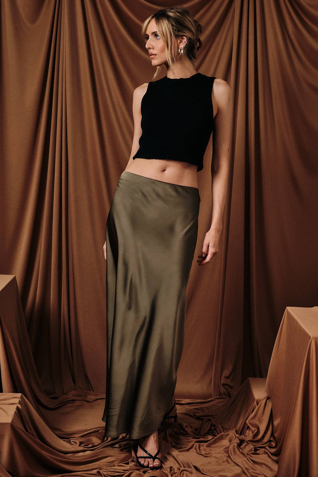 A bias-cut satin midi skirt in olive, worn by a model with a black top.