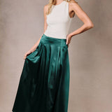 Woman wearing a hunter green satin midi skirt with a high waist and fuller silhouette.