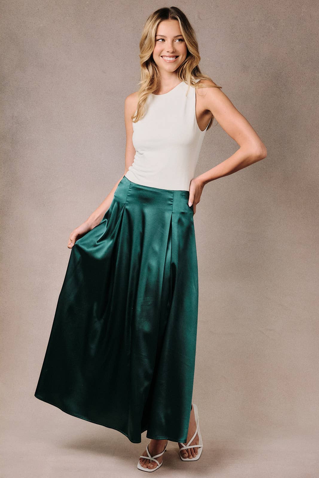 Woman wearing a hunter green satin midi skirt with a high waist and fuller silhouette.